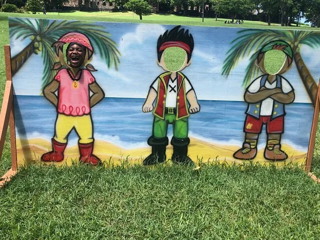 A child smiles through a cutout in a pirate-themed wooden photo board.