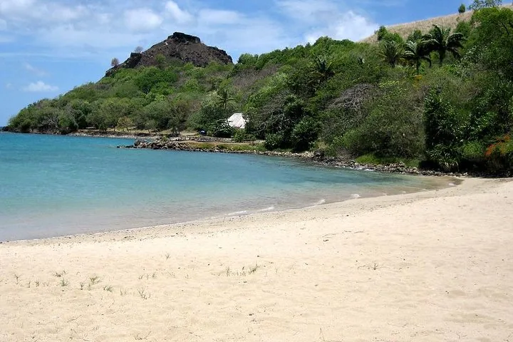 Empty sandy beach with clear water and lush green hills in the background.