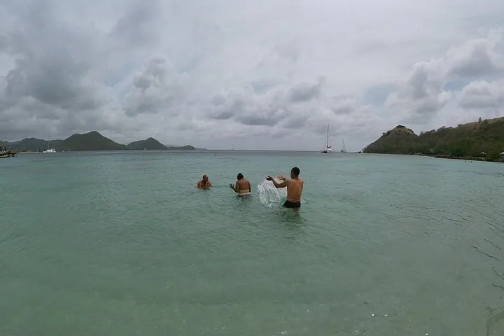 People playing and splashing in the ocean water with boats in the background.