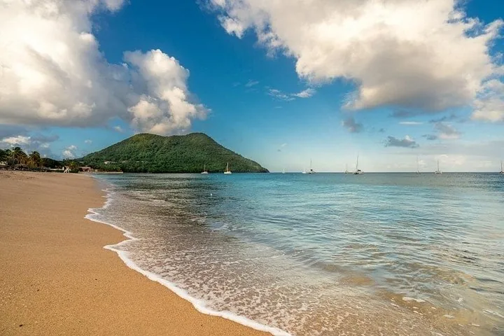 A serene beach with gentle waves and a green hill in the distance.
