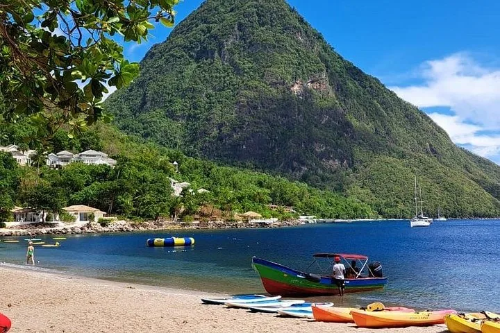 A colorful boat on a sandy beach with a large green mountain behind.