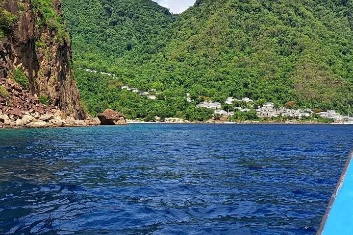 A view from the water showing a rocky coastline and green hillside homes.