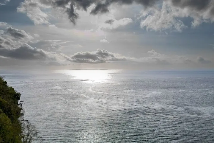 Sunlight reflects on the ocean water under a cloudy, overcast sky.