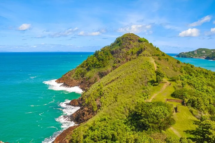 Scenic view of a verdant coastal hill meeting the vibrant turquoise ocean waters.