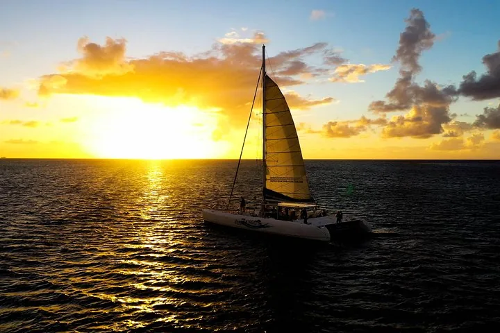 Silhouette of a catamaran sailing on the ocean during a golden sunset.